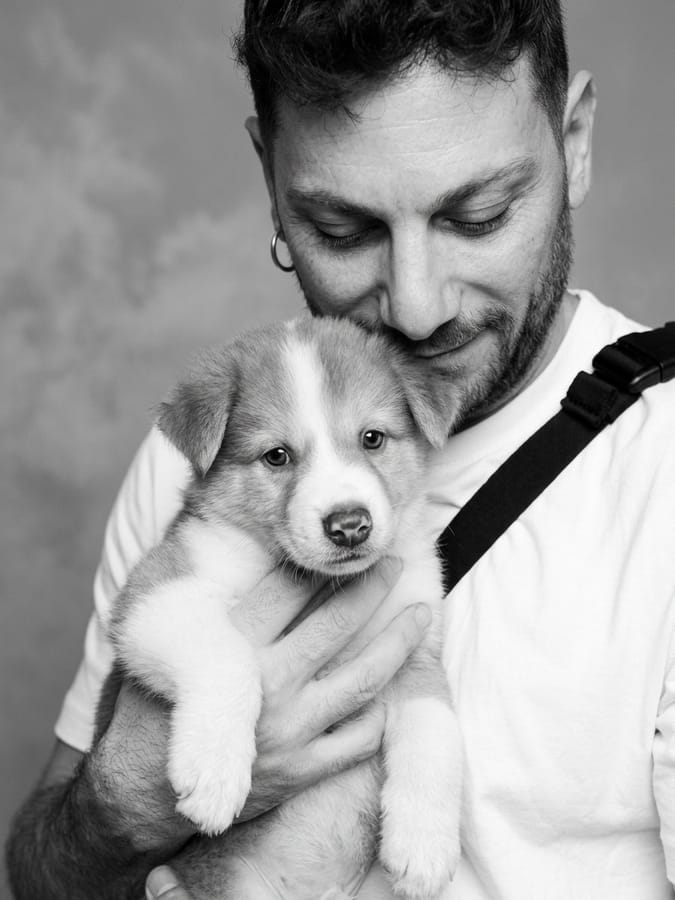 Ritratto in bianco e nero a luce chiara dello stesso uomo con il cucciolo in braccio, fondo di studio morbido